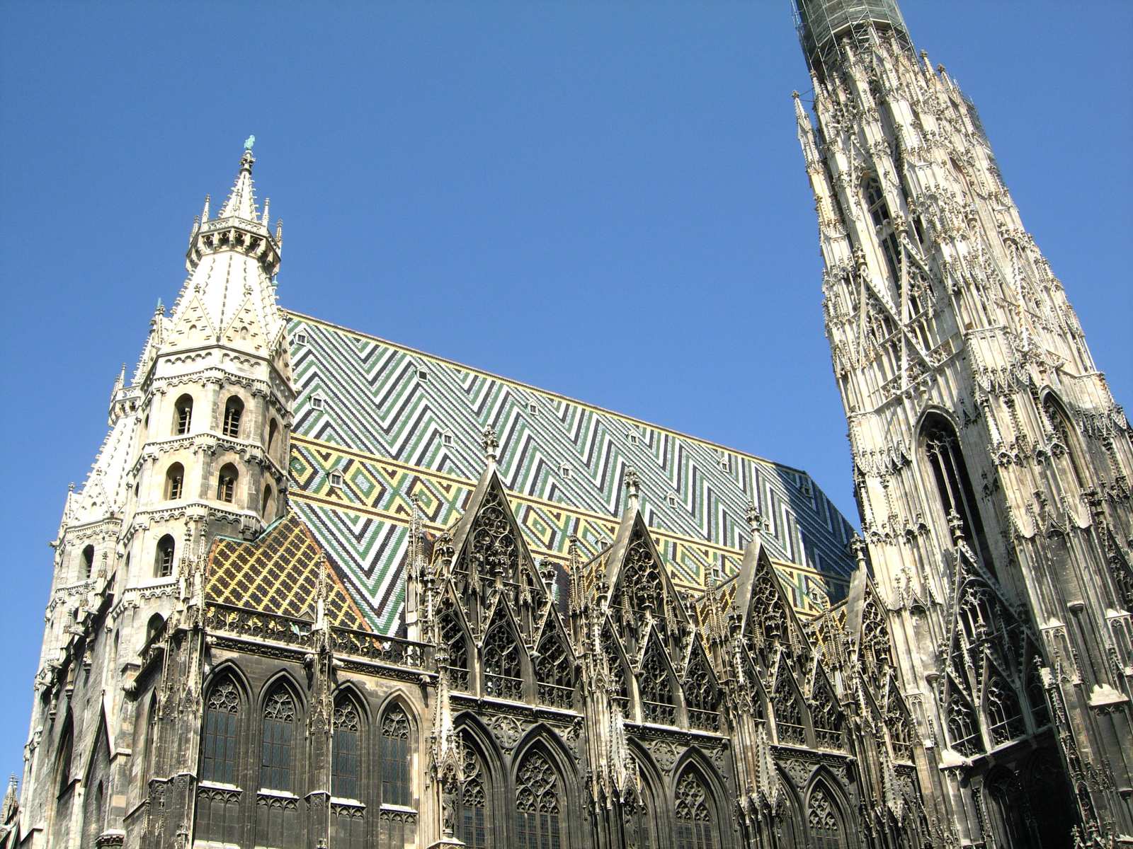 Stephansdom cathedral in Vienna with its distinctive diamond-patterned tiled roof and Gothic spires against a clear blue sky