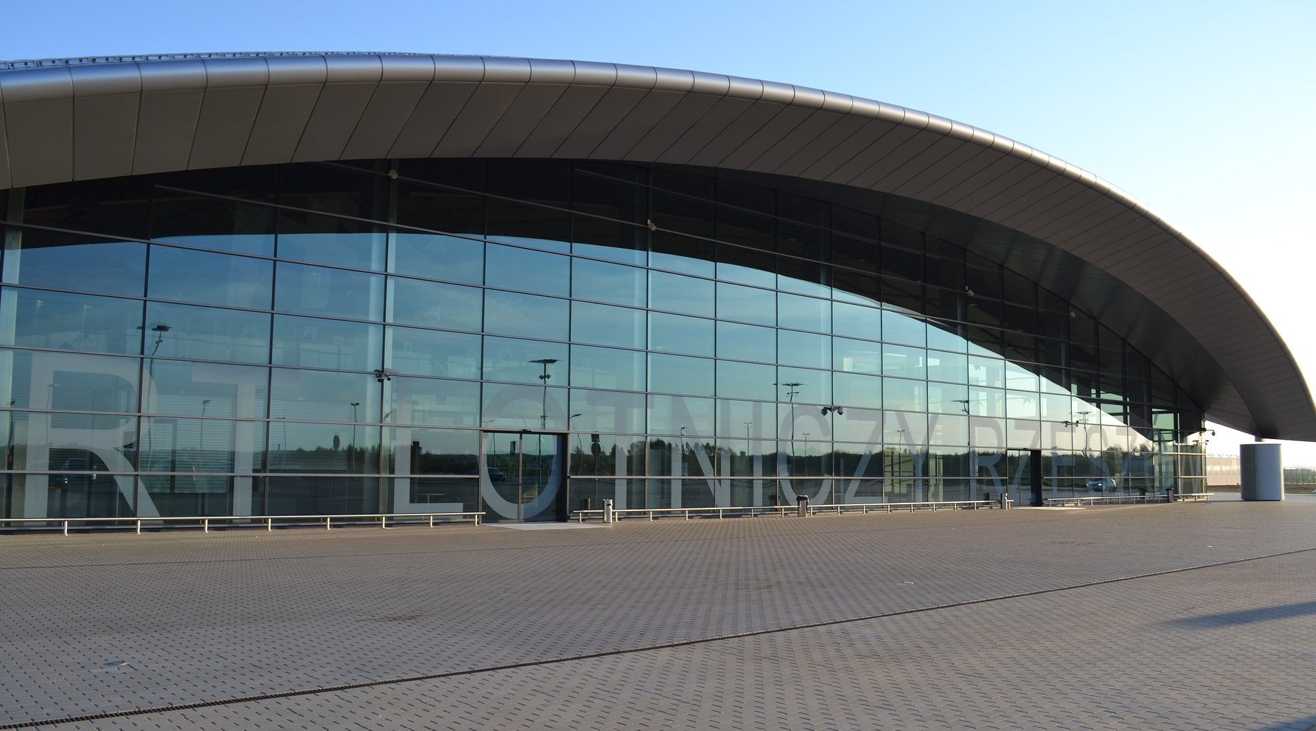 The glazed facade and curved roof of the Rzeszów-Jasionka passenger terminal in low evening sun