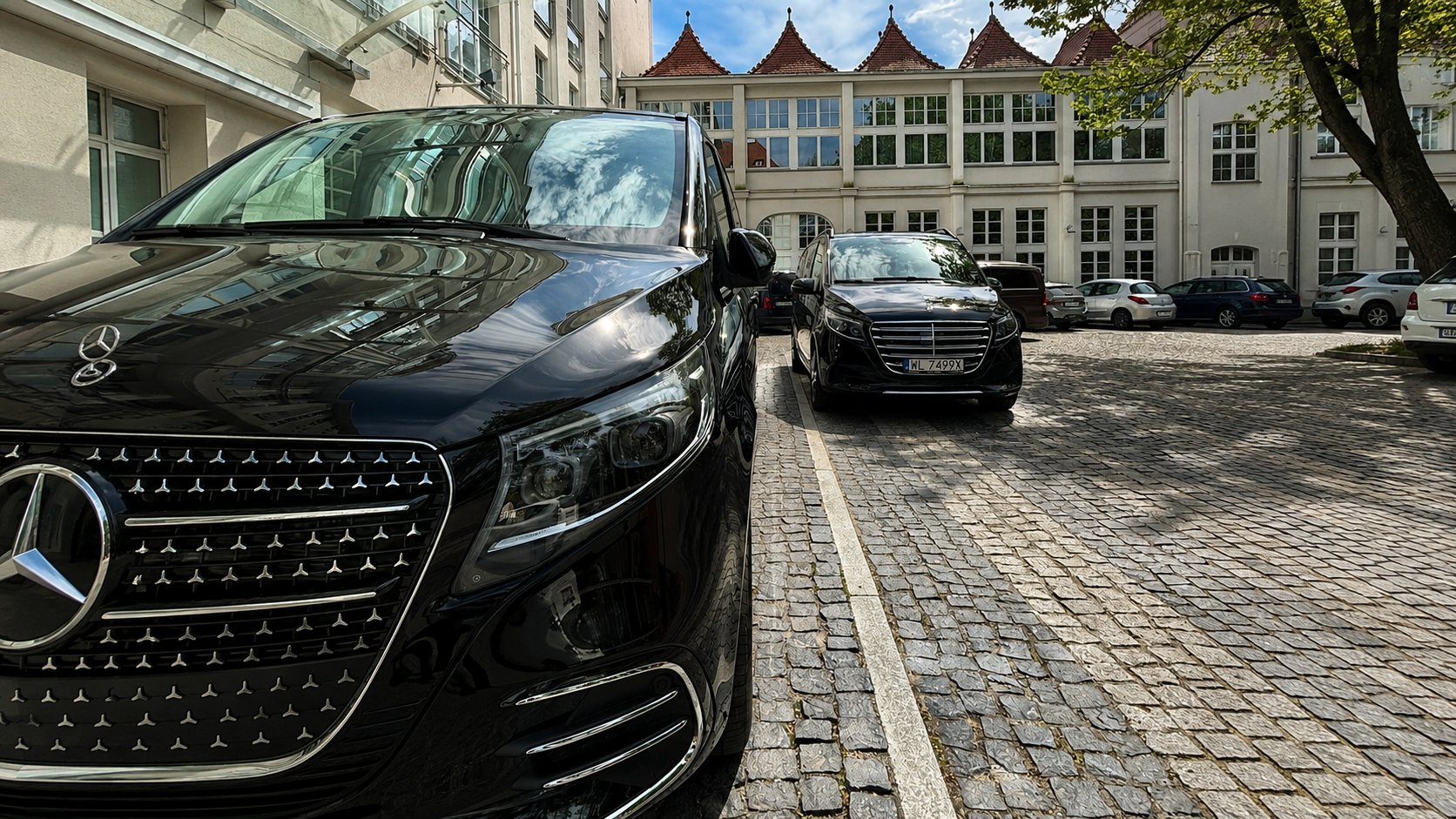 Two black Mercedes-Benz V-Class chauffeur vans parked in a cobbled courtyard