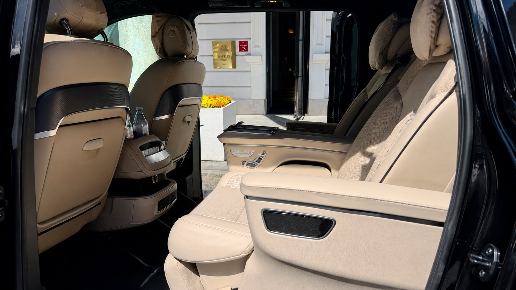 Cream leather cabin of a Mercedes-Benz V-Class First Class, seen through the open sliding door outside a hotel entrance